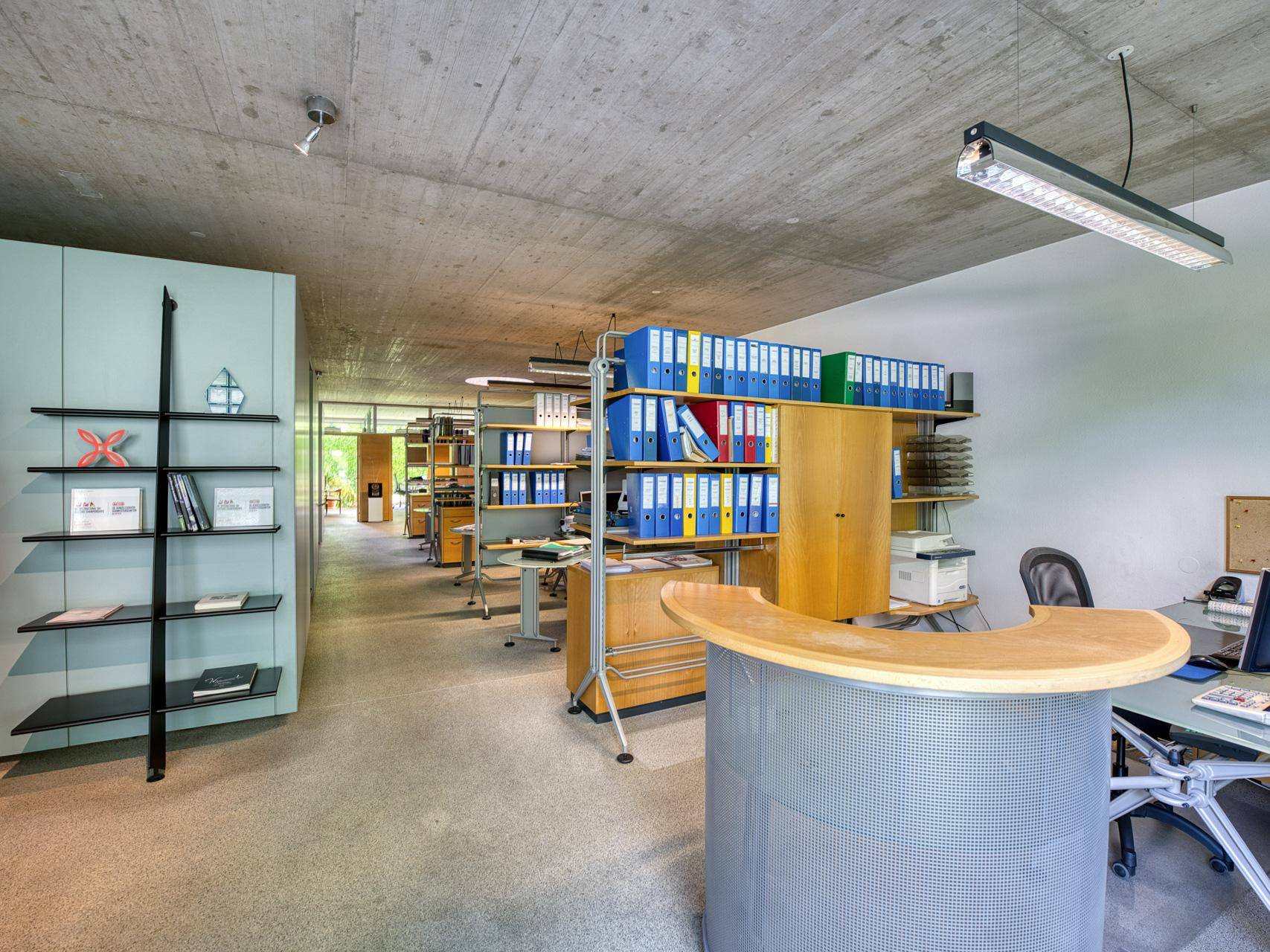 Geräumiges Büro mit vielen Aktenregalen, Empfangstheke und Sichtbetondecke.