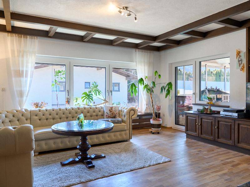 Helles Wohnzimmer mit großen Fenstern, Holzbalkendecke und einem eleganten beigen Sofa, das zum Entspannen einlädt.