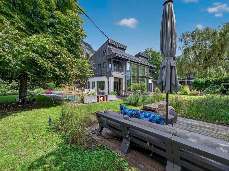 Weitläufiger Gartenbereich mit modernem Haus, Pool und gemütlicher Lounge-Ecke vor Bergpanorama.