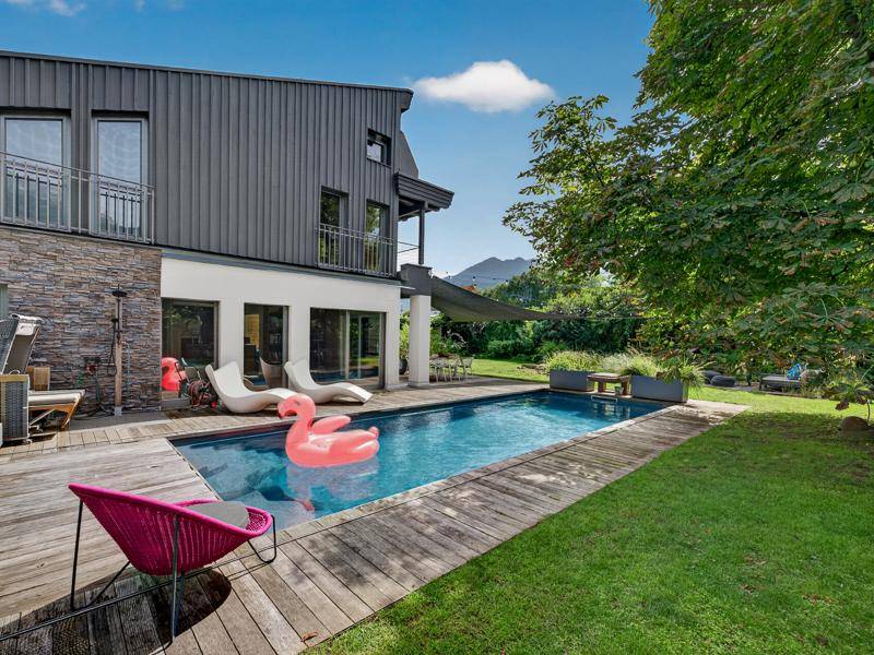Ansicht des modernen Hauses mit Pool, Holzdeck und gepflegtem Gartenbereich unter blauem Himmel.