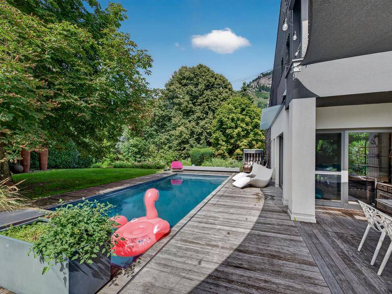 Moderner Swimmingpool mit Holzdeck und Liegeflächen, umgeben von üppigem Grün und Bäumen.