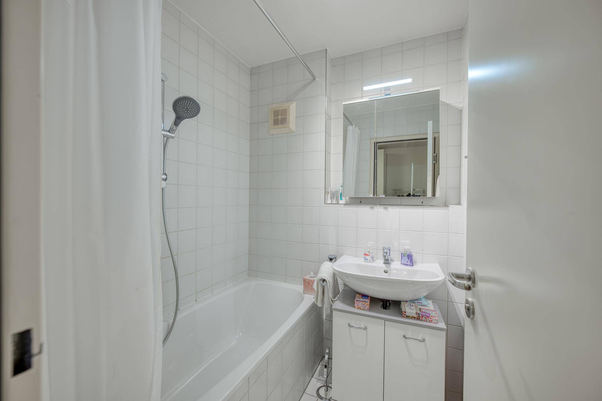 Funktionales Badezimmer mit Badewanne, Duschfunktion und weiß gefliesten Wänden.