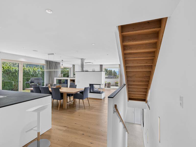 Offener Wohnbereich mit Holzboden, Esstisch und einer eleganten Holztreppe, die in die obere Etage führt.