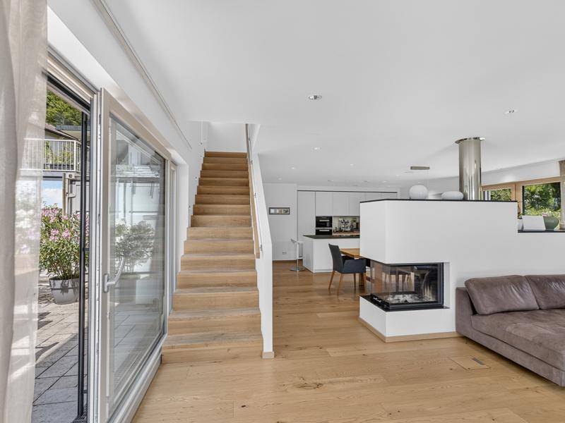 Helles Wohnzimmer mit Holzboden, Kamin und großen Glasschiebetüren, die zur sonnigen Terrasse führen.