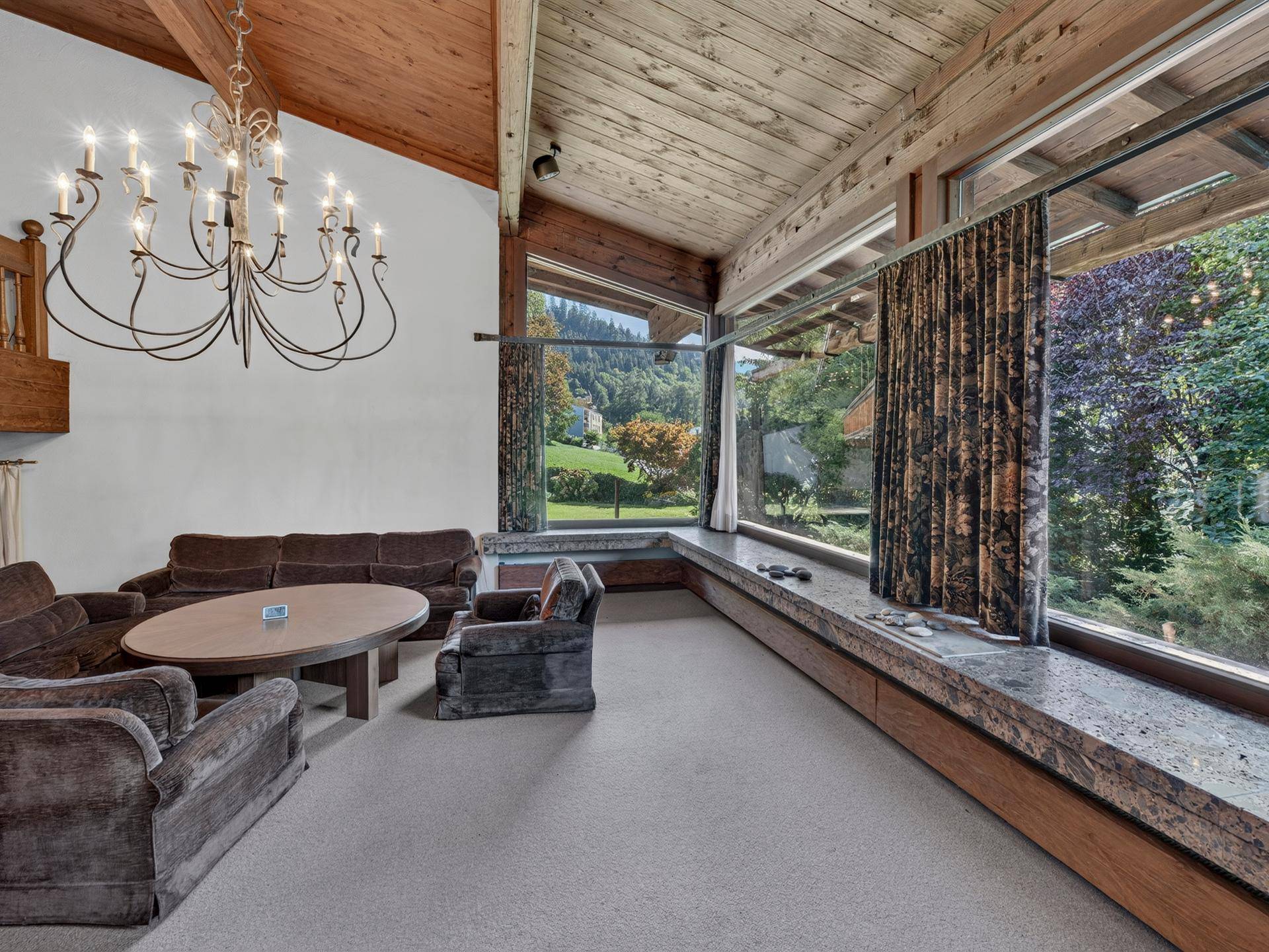 Helles Wohnzimmer mit hohen Holzdecken, großen Panoramafenstern und Blick ins Grüne.