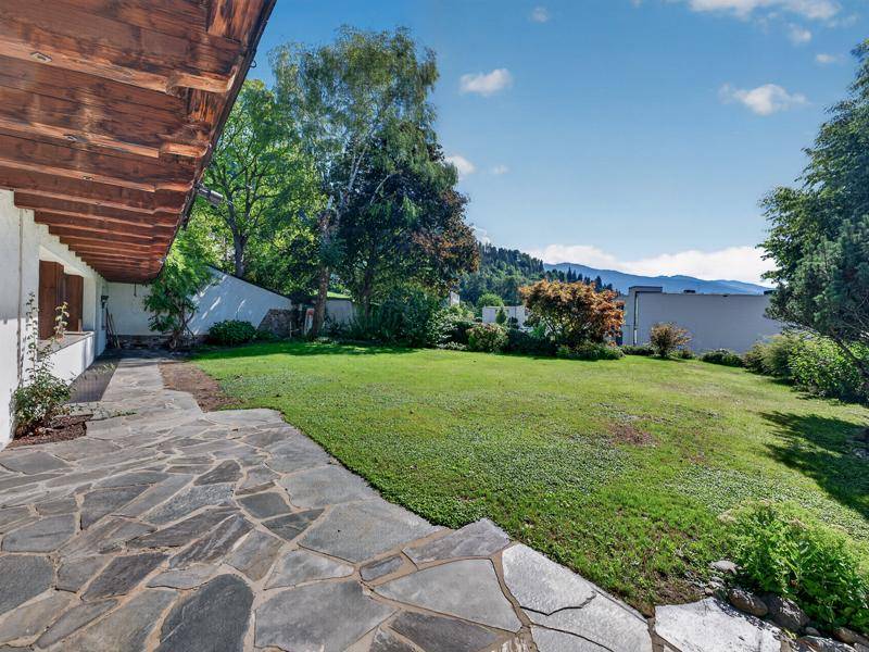Weitläufiger Garten mit Naturstein-Terrasse, Rasenfläche und Fernblick auf die Berge.