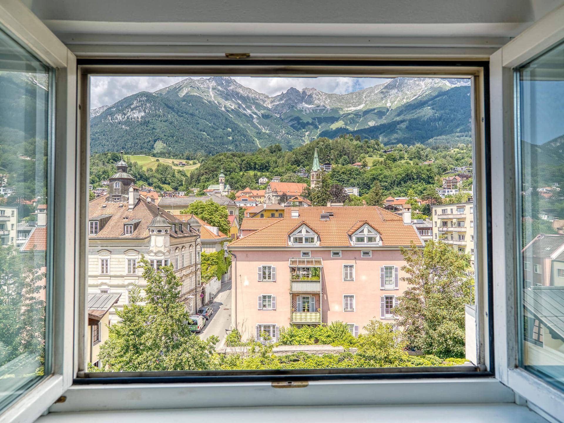 Malerischer Ausblick aus dem Fenster auf die Stadt mit traditionellen Gebäuden und majestätischen Bergen.