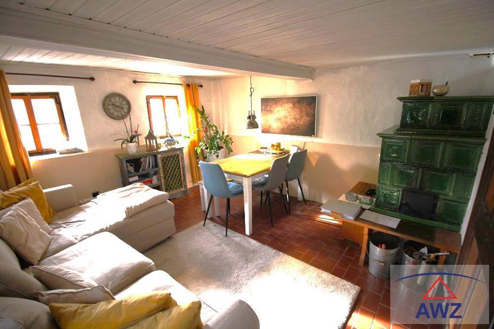 Gemütlicher Wohn-Essbereich mit traditionellem Kachelofen, Holzbalken und Terrakottafliesen.