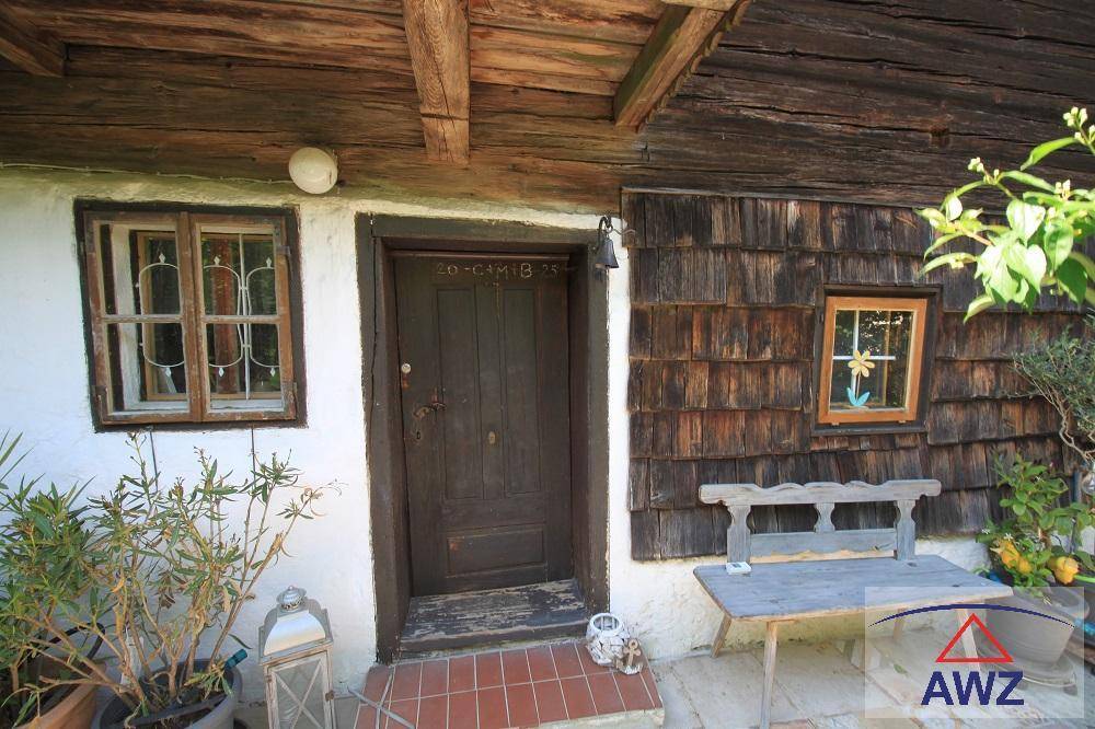 Rustikaler Hauseingang mit Holztür und kleinen Fenstern, umgeben von Topfpflanzen.