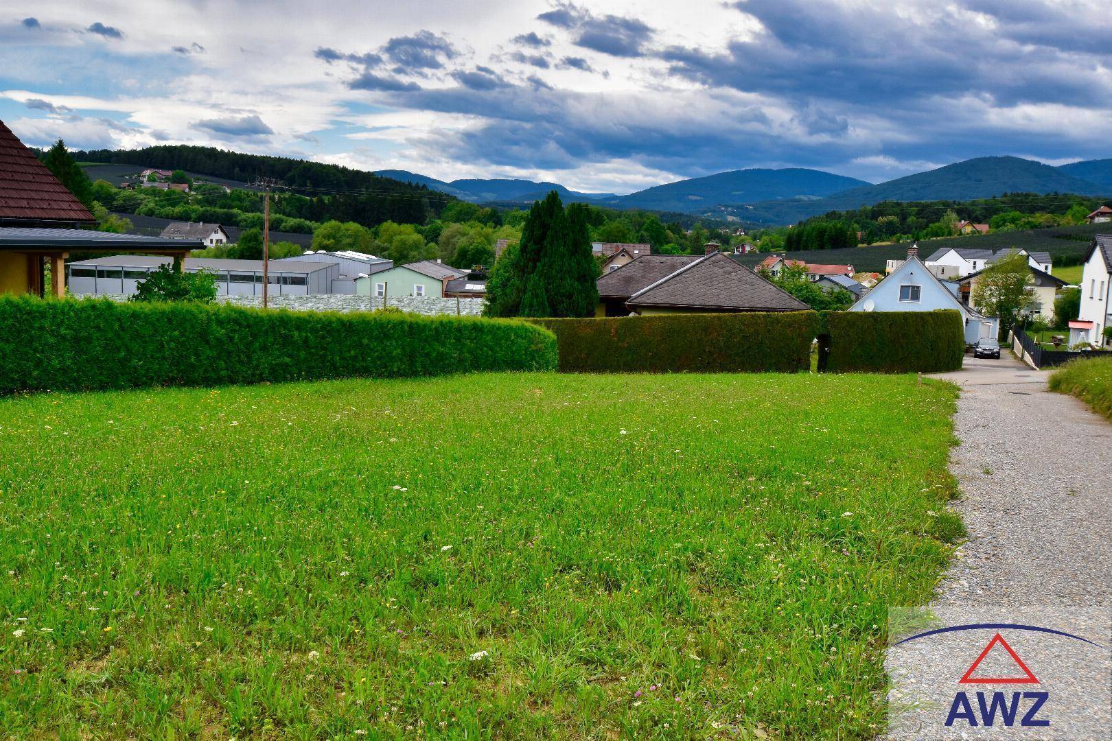Grüne Außenfläche mit Hecke, umgeben von Häusern und einem weiten Blick auf die Berge.