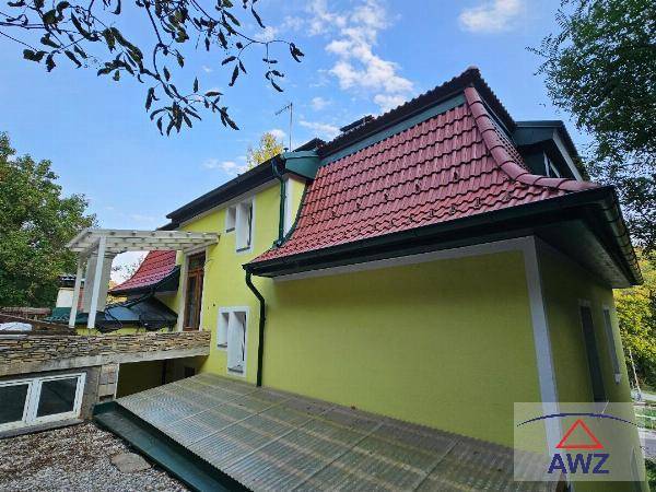 Seitenansicht des Hauses mit rotem Ziegeldach und einer überdachten Terrasse im oberen Bereich.