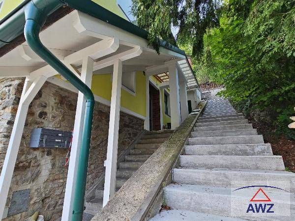 Lange Außentreppe führt zum Eingang des Hauses, umgeben von Bäumen und Grün.