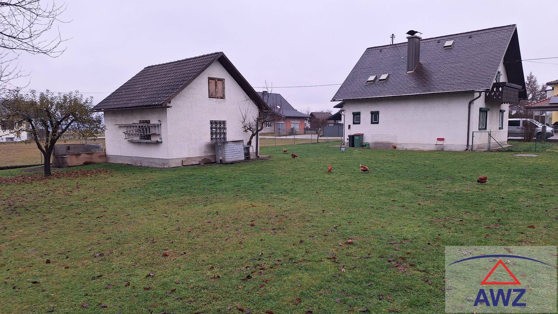 Große Rasenfläche mit zwei Wohnhäusern im Hintergrund, umgeben von ländlicher Natur.