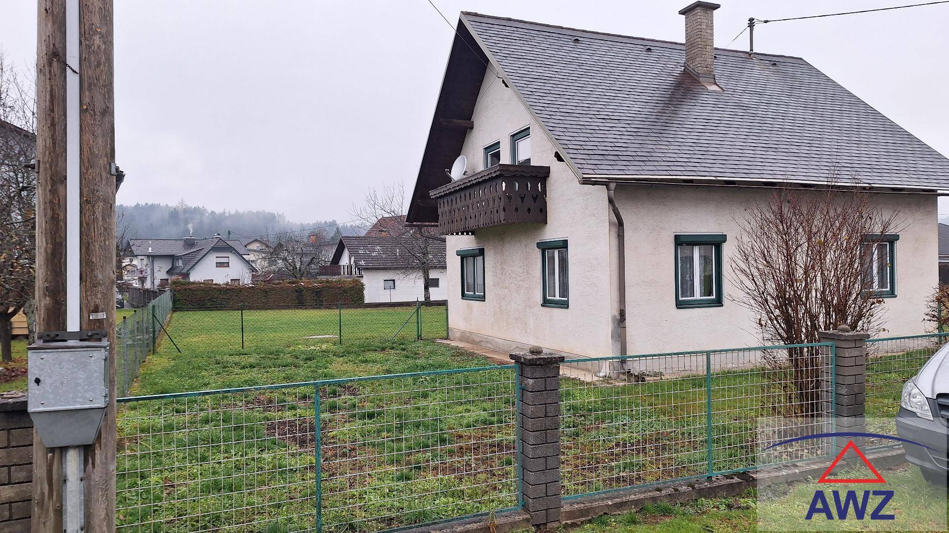 Seitenansicht des Hauses mit kleinem Balkon, grünen Fensterläden und umzäuntem Gartenbereich.