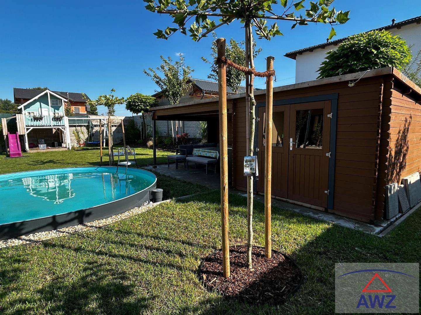 Gepflegter Garten mit kleinem Pool, Gartenhaus und jungem Baum an einem sonnigen Tag.