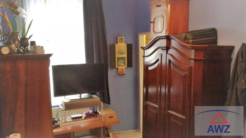 Schlafzimmer mit großem Holzschrank, Fernseher und dunklen Vorhängen vor dem Fenster.