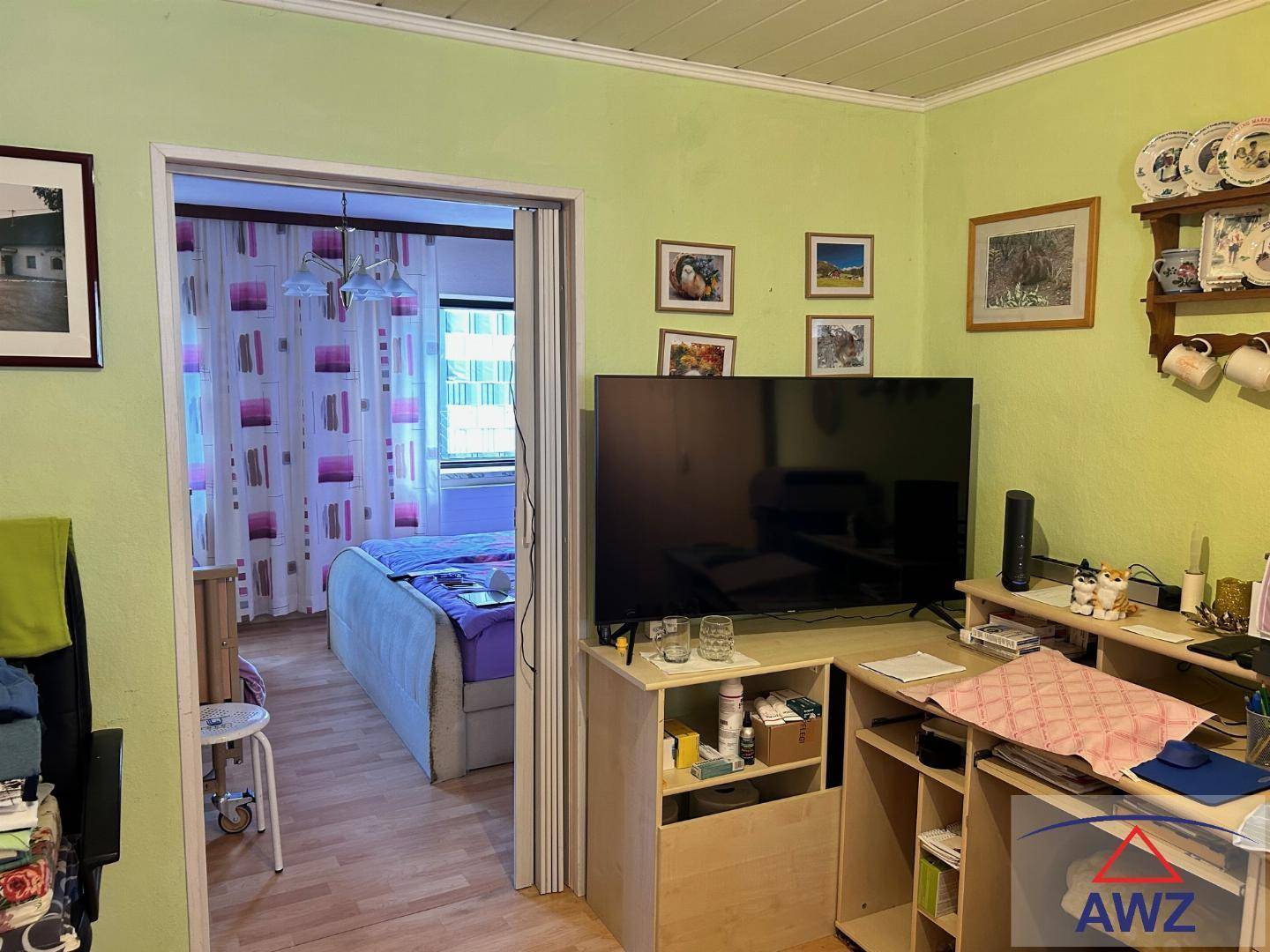 Helles Wohnzimmer mit Fernseher und Zugang zu einem angrenzenden Schlafzimmer.