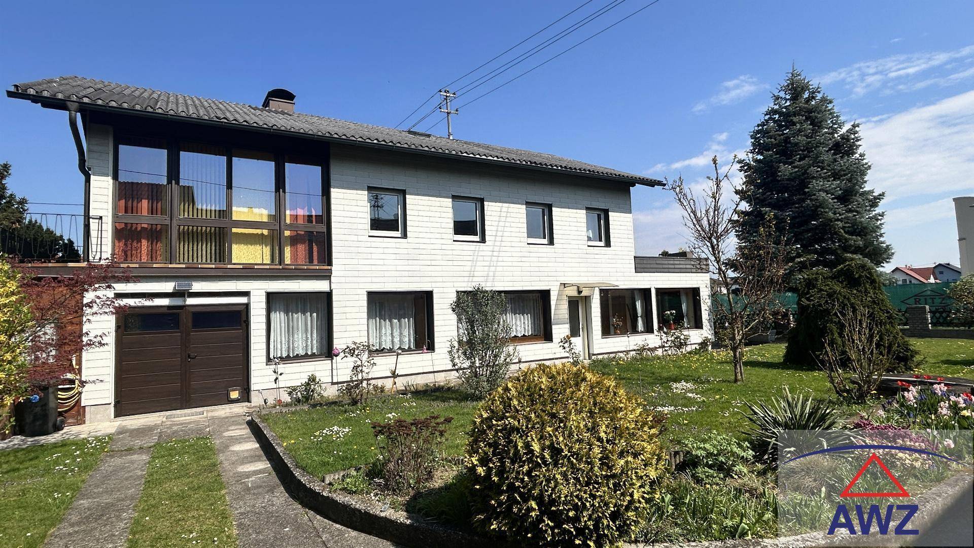 Freistehendes Einfamilienhaus mit Garage, gepflegtem Vorgarten und Zufahrt bei sonnigem Wetter.