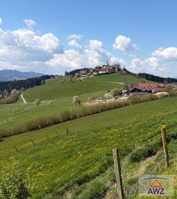 Weitläufige grüne Hügellandschaft mit einem malerischen Dorf auf dem Berg und weitem Blick.