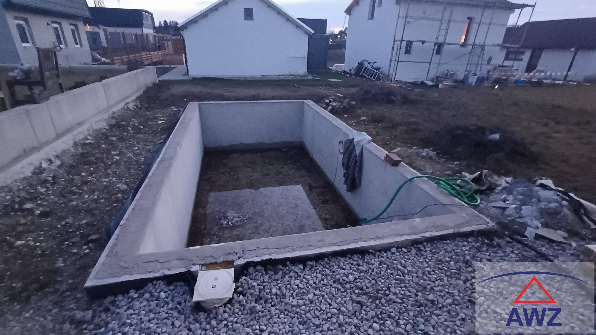 Ausgehobene Grube mit Betonwänden, möglicherweise für einen Pool oder Keller, auf einer Baustelle.
