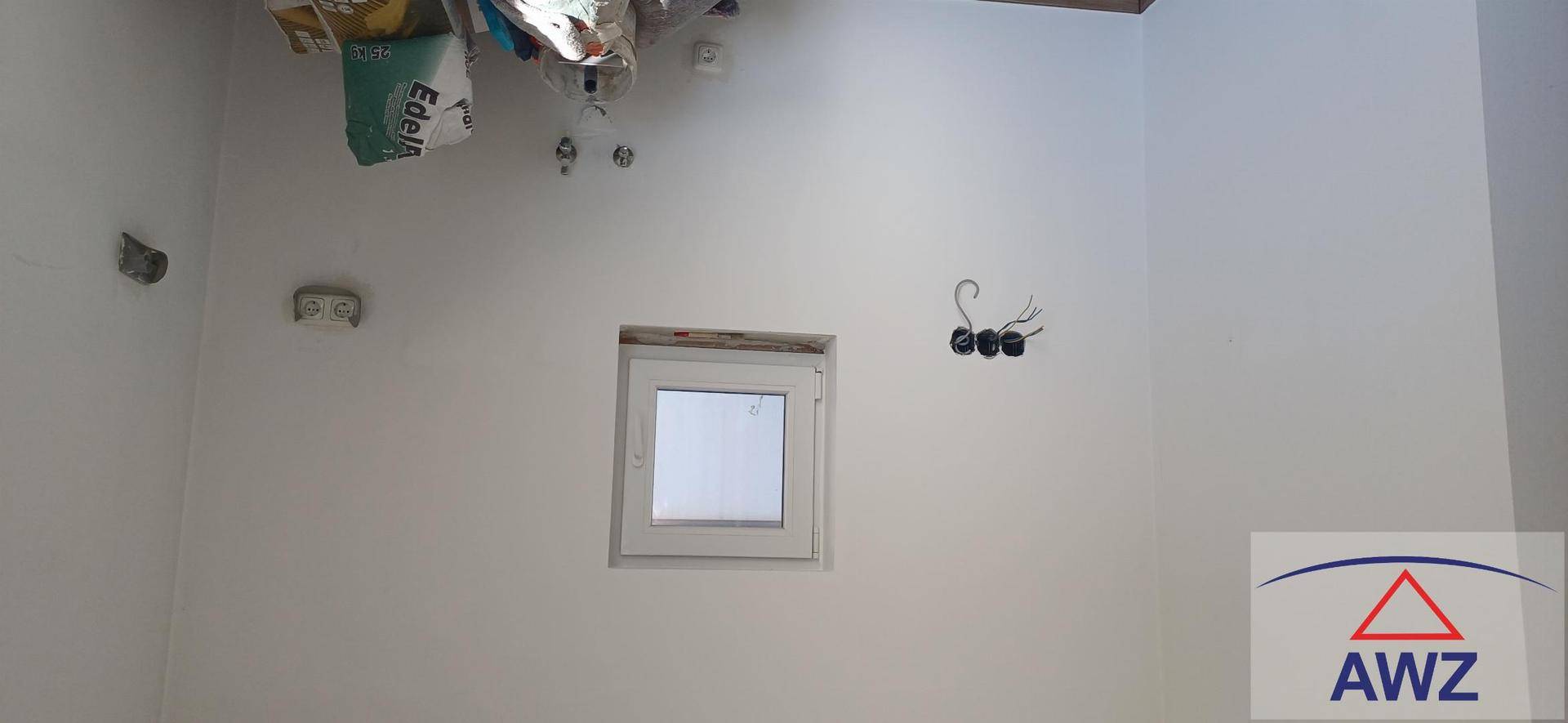 Innenraum im Rohbau mit weiß gestrichenen Wänden, kleinem Fenster und sichtbaren Elektroinstallationen.