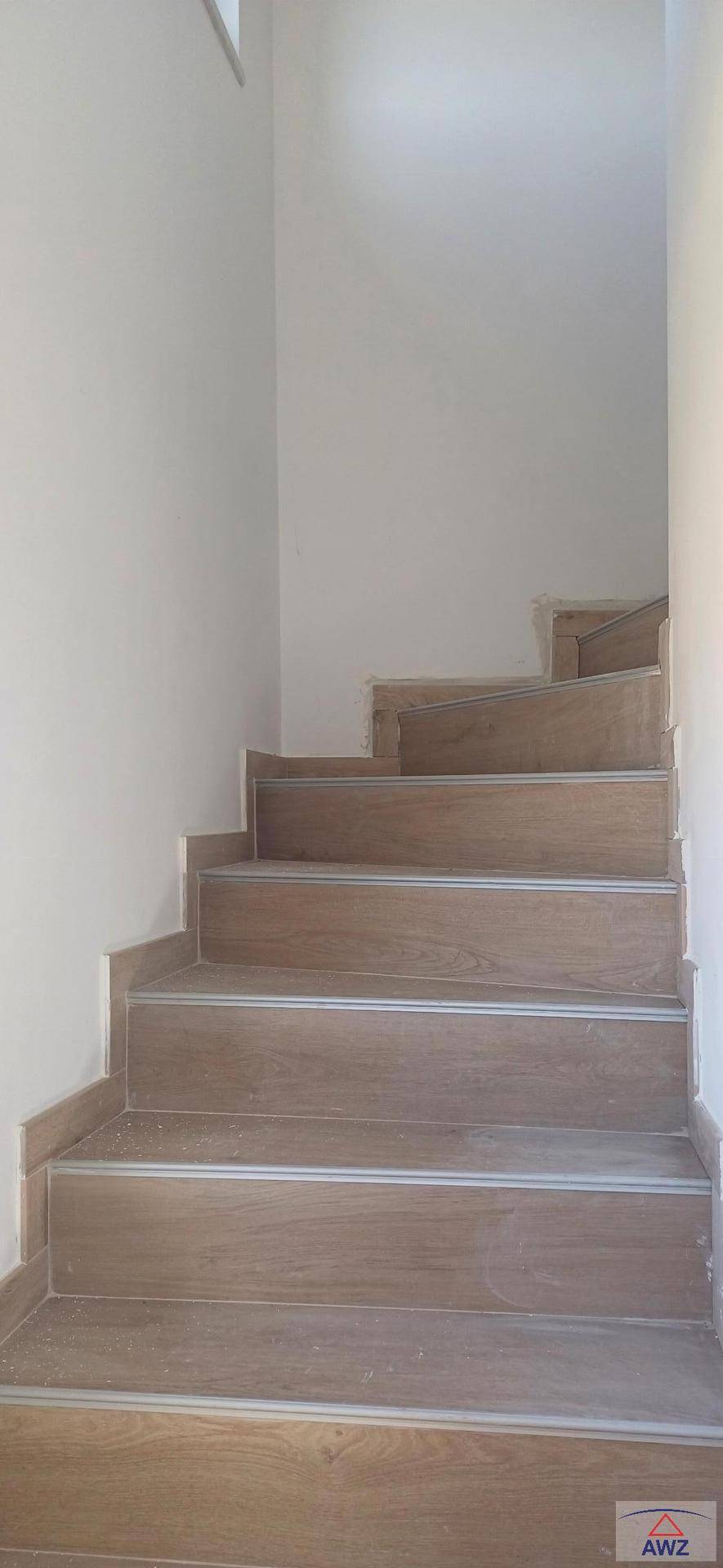 Moderne Treppe mit Holzoptik-Fliesen und schlichten weißen Wänden im Innenbereich.