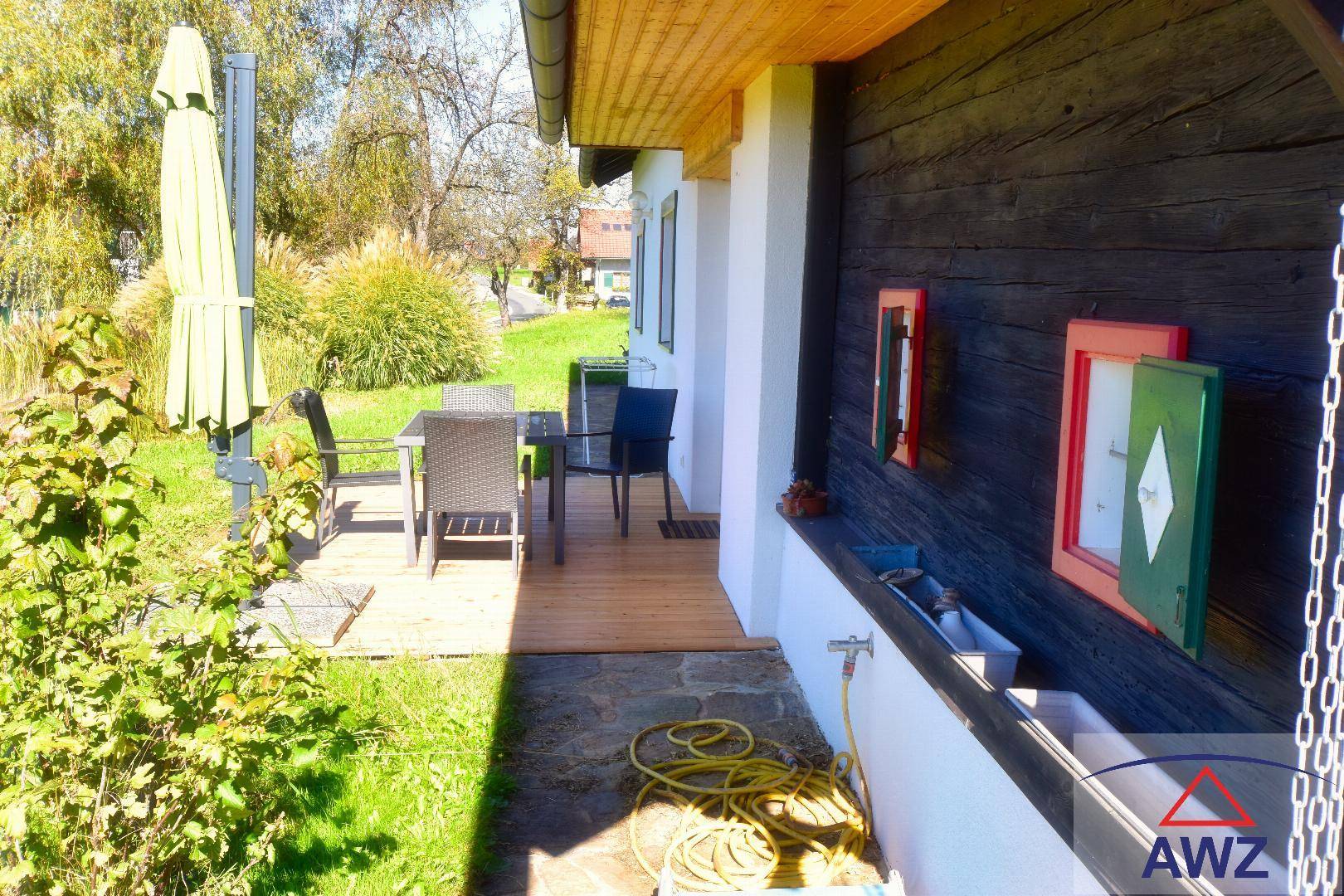 Seitliche Terrasse mit Holzbelag, Sonnenschirm und Blick in den Garten.