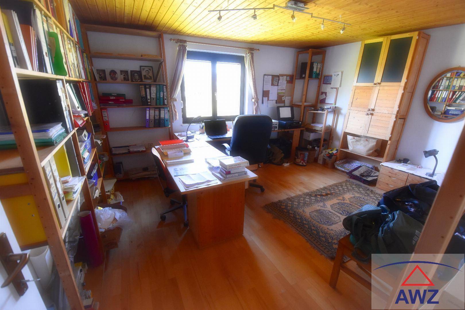 Geräumiges Arbeitszimmer mit Holzdecke, vielen Regalen und großem Fenster.