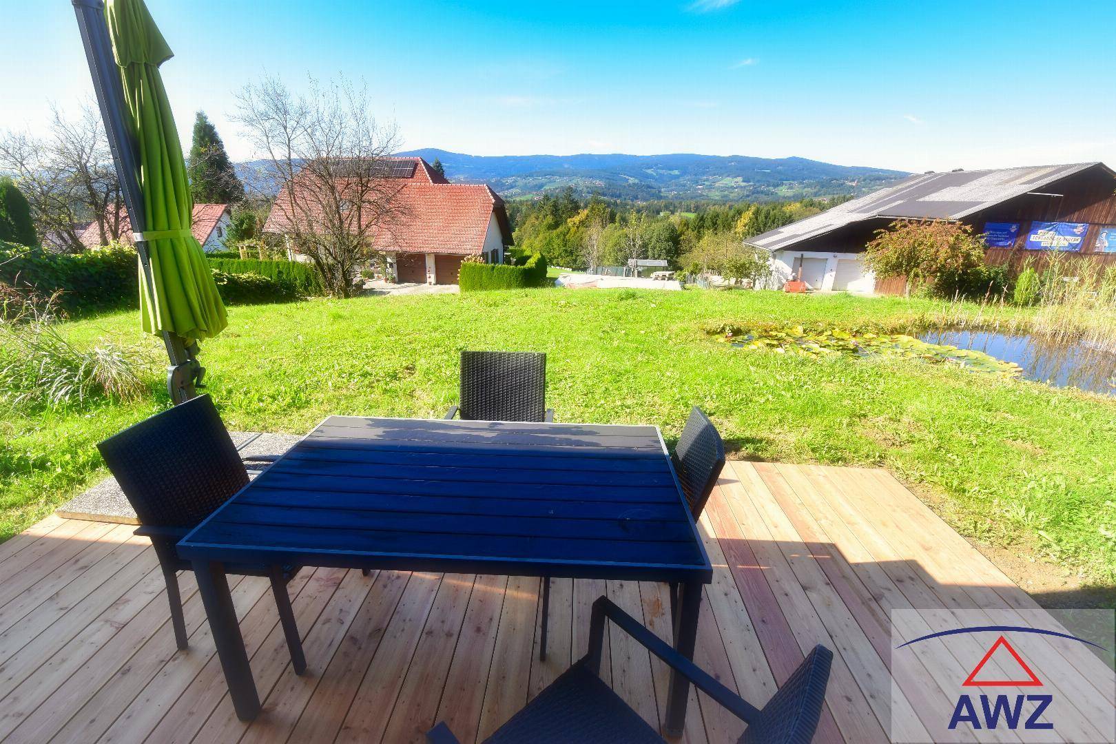 Sonnige Holzterrasse mit Sitzgelegenheiten, Teich und weitem Bergblick.