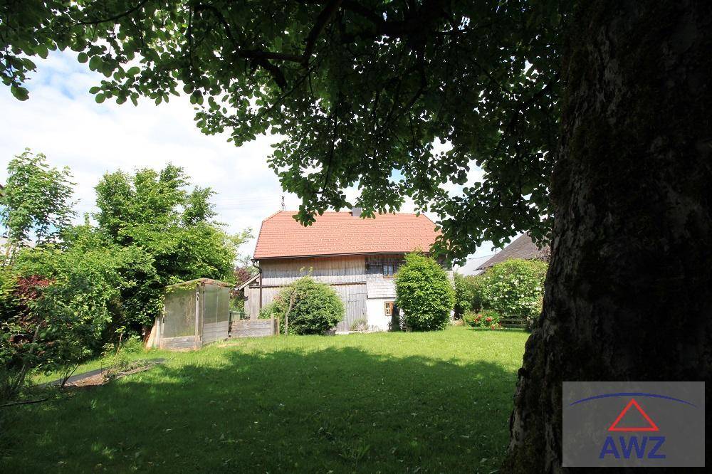Weitläufiger grüner Garten mit altem Baumbestand und Blick auf das traditionelle Holzhaus im Hintergrund.