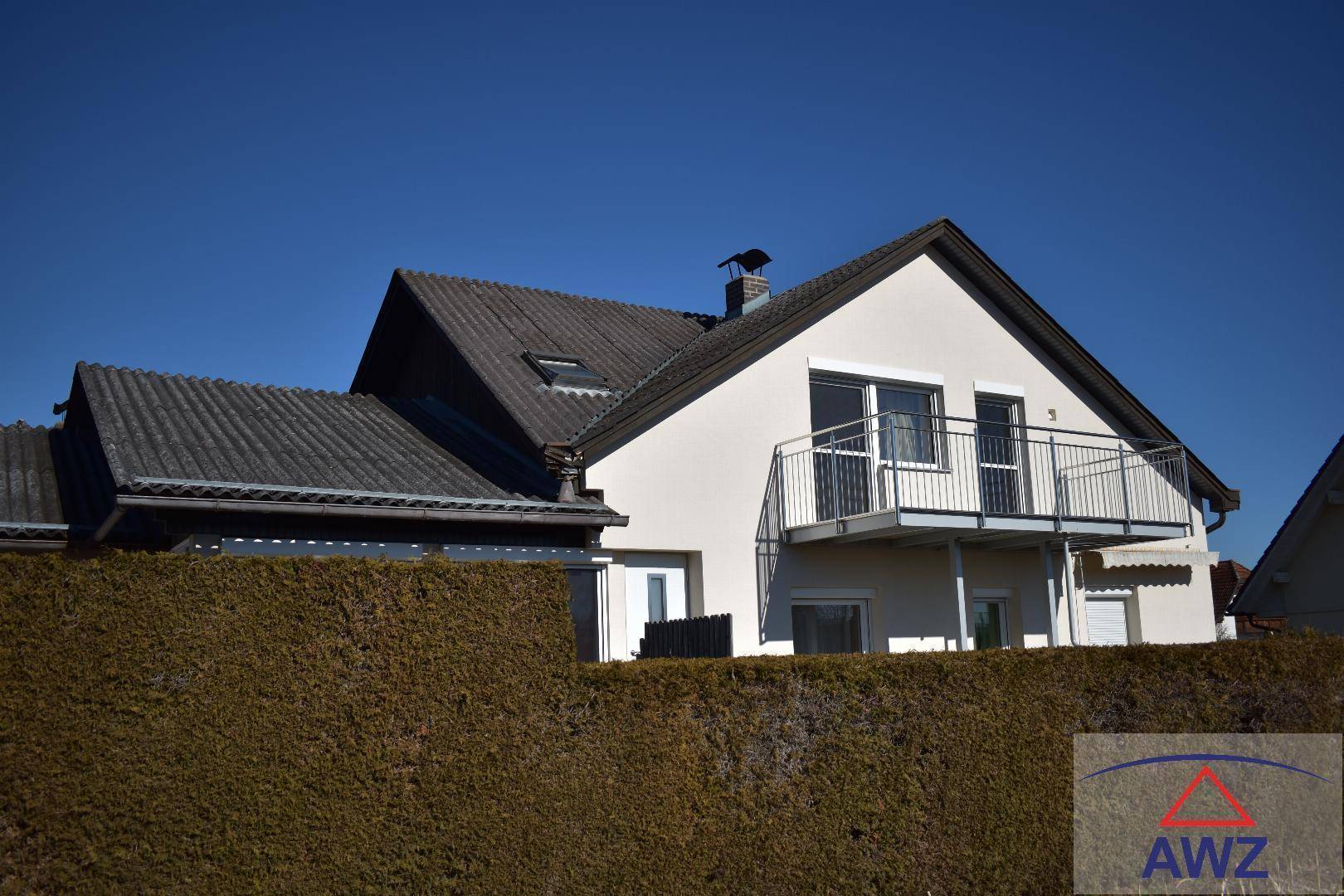 Rückansicht des Hauses mit Balkon, dunklem Dach und gepflegter Hecke.