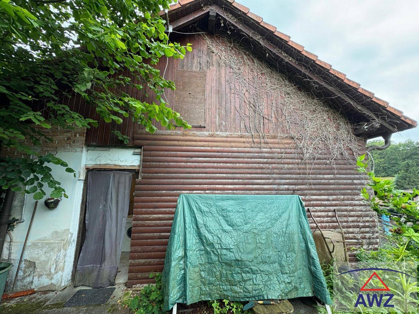 Rustikale Holzfassade eines Gebäudes mit Ziegeldach und Bewuchs, teilweise abgedeckt.
