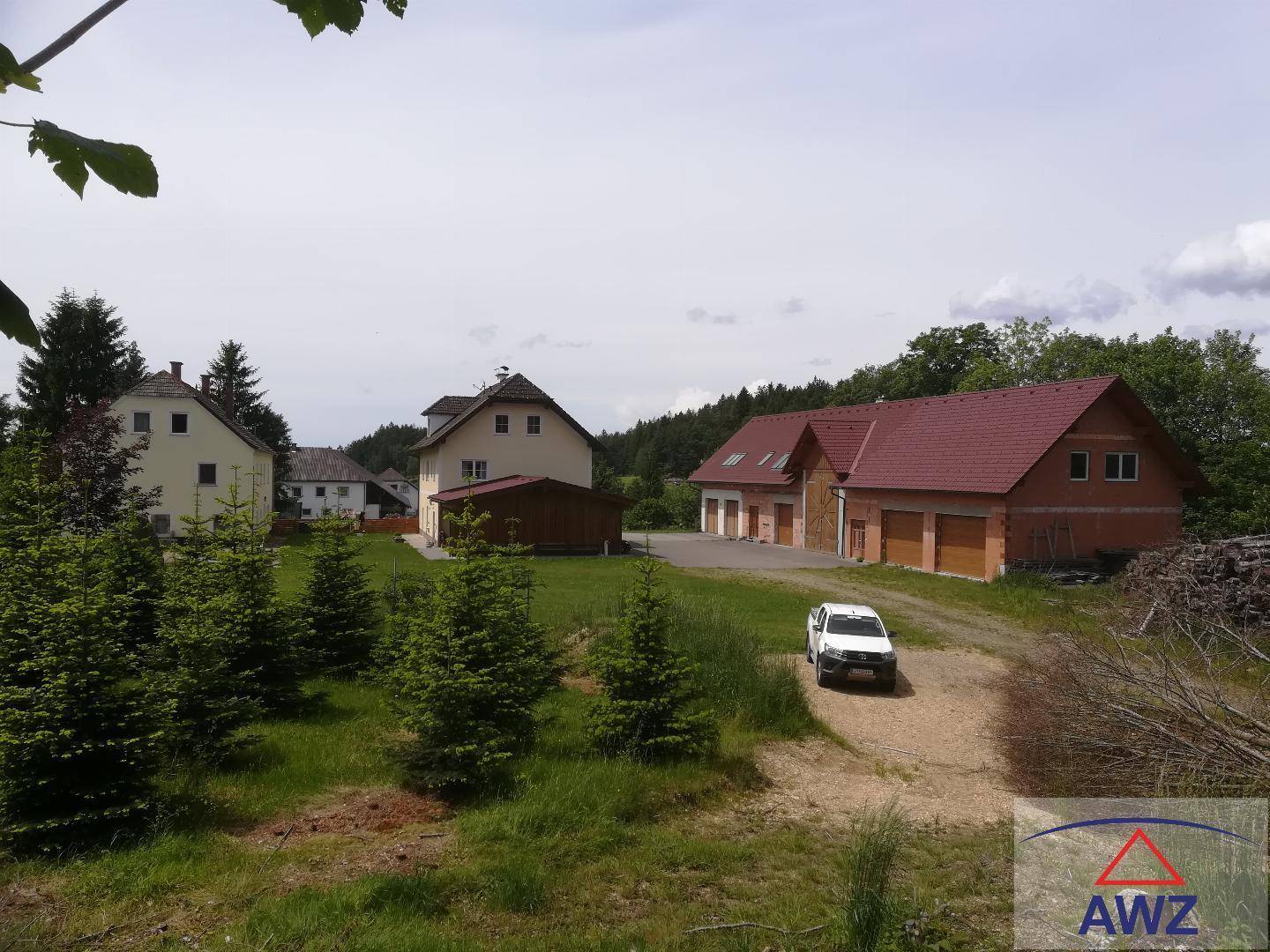 Mehrere Gebäude in ländlicher Umgebung mit weiten Grünflächen und Wald im Hintergrund.