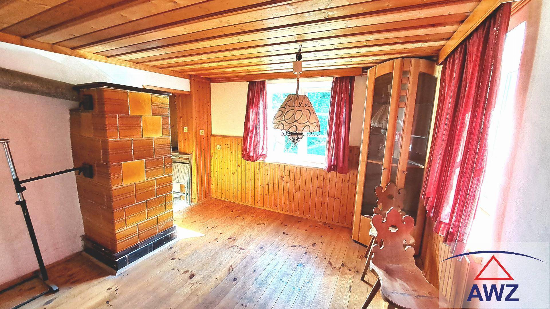 Gemütliches Wohnzimmer mit Holzboden, Holzvertäfelung und einem traditionellen Kachelofen.