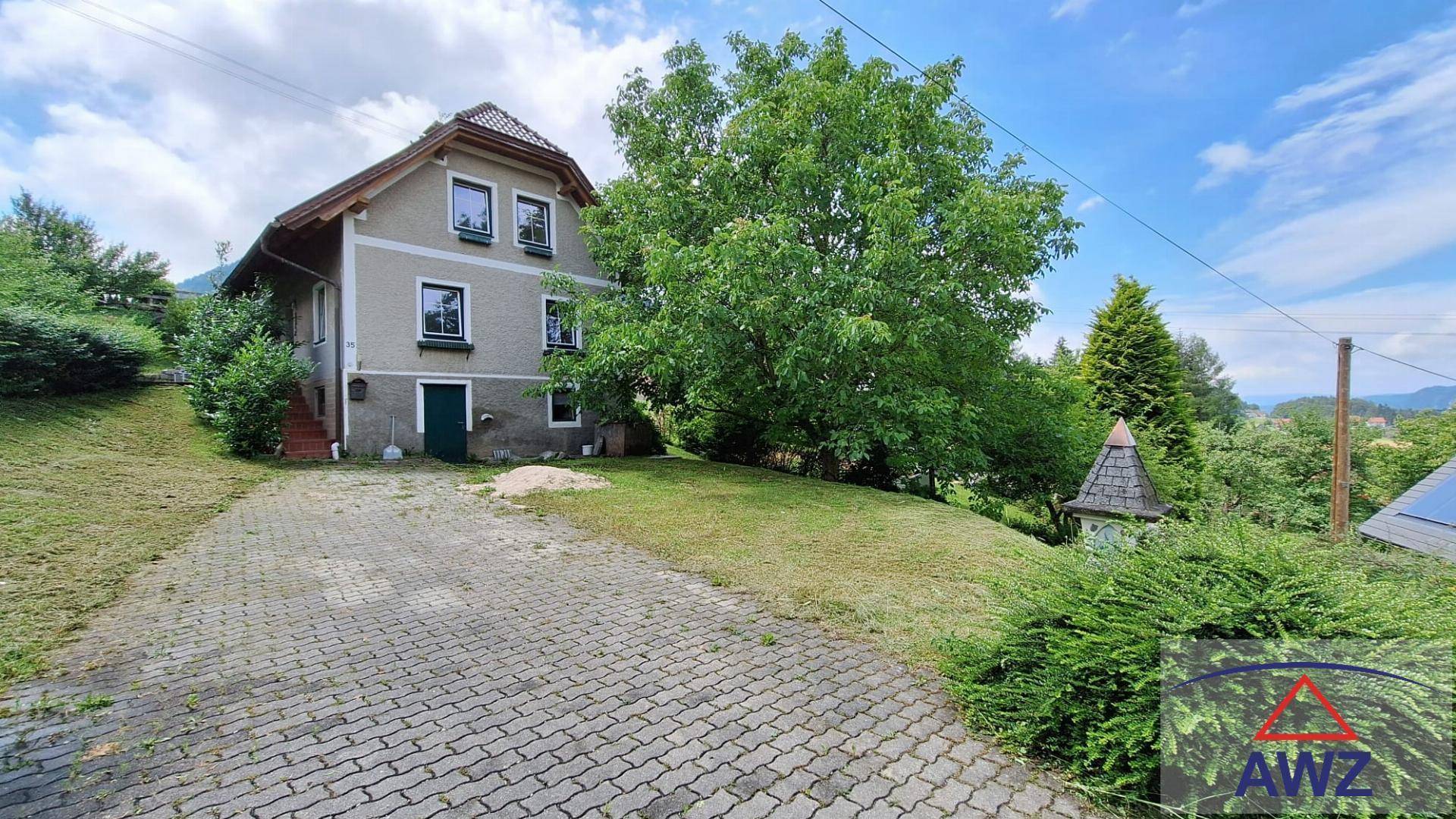 Vorderansicht des Hauses mit gepflasterter Auffahrt, großem Baum und grüner Umgebung.