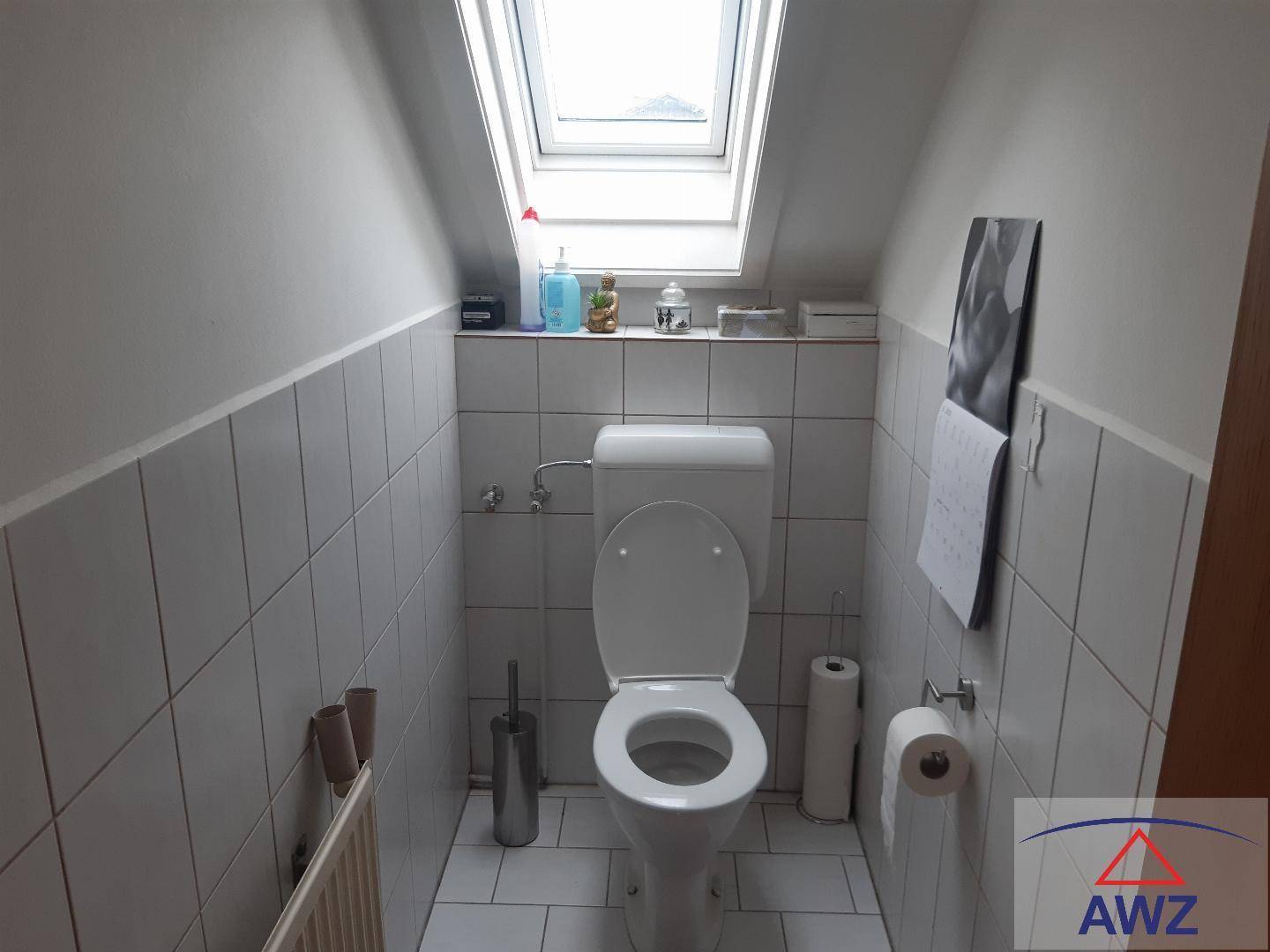Kleines WC mit Dachfenster, hellen Fliesen und schräger Decke.