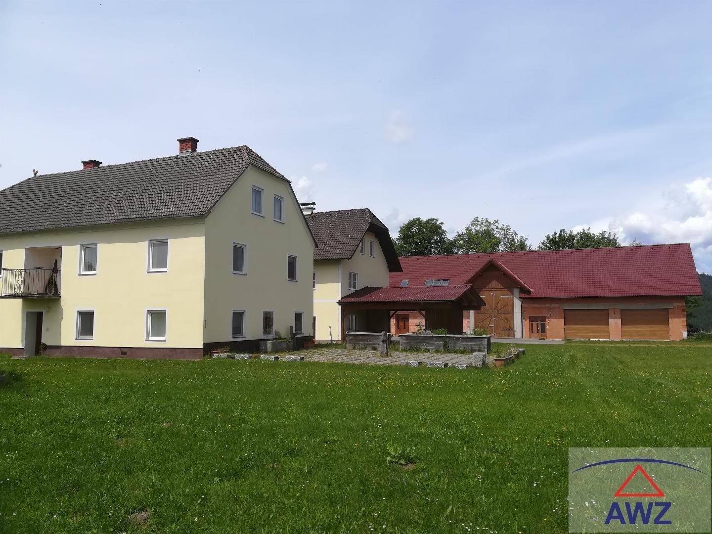 Ländliches Anwesen mit mehreren Gebäuden, darunter ein Wohnhaus und Garagen, umgeben von Grünflächen.