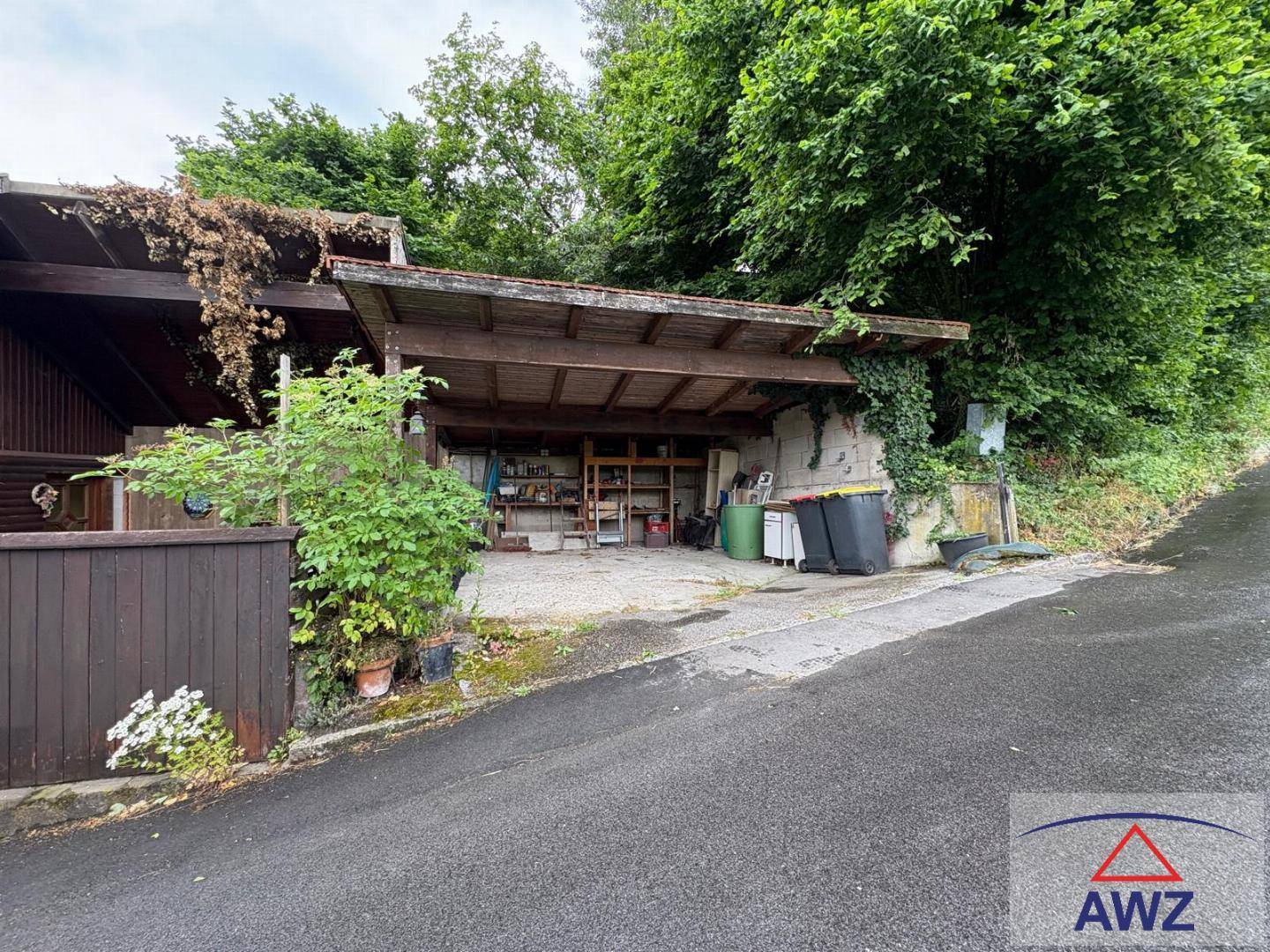 Außenansicht eines Holzcarports mit Lagerbereich und angrenzender Natur an einer Hanglage.