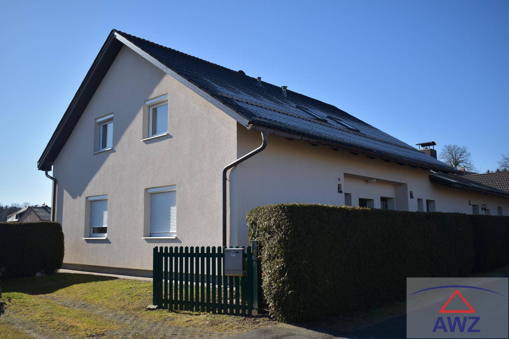 Modernes Einfamilienhaus mit heller Fassade, dunklem Dach und Photovoltaikanlage.