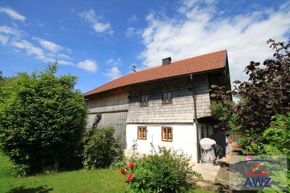 Charmantes Holzhaus mit traditioneller Architektur, rotem Ziegeldach und umgebendem grünen Garten unter blauem Himmel.