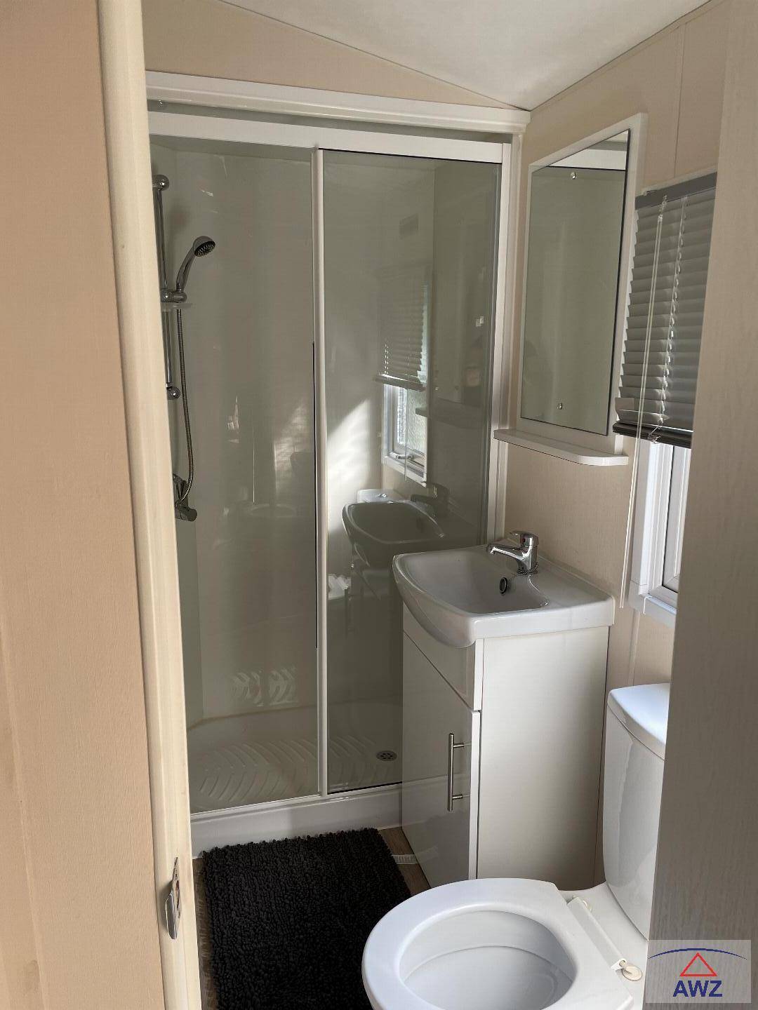 Kleines Badezimmer mit Duschkabine, Waschbecken und Toilette.