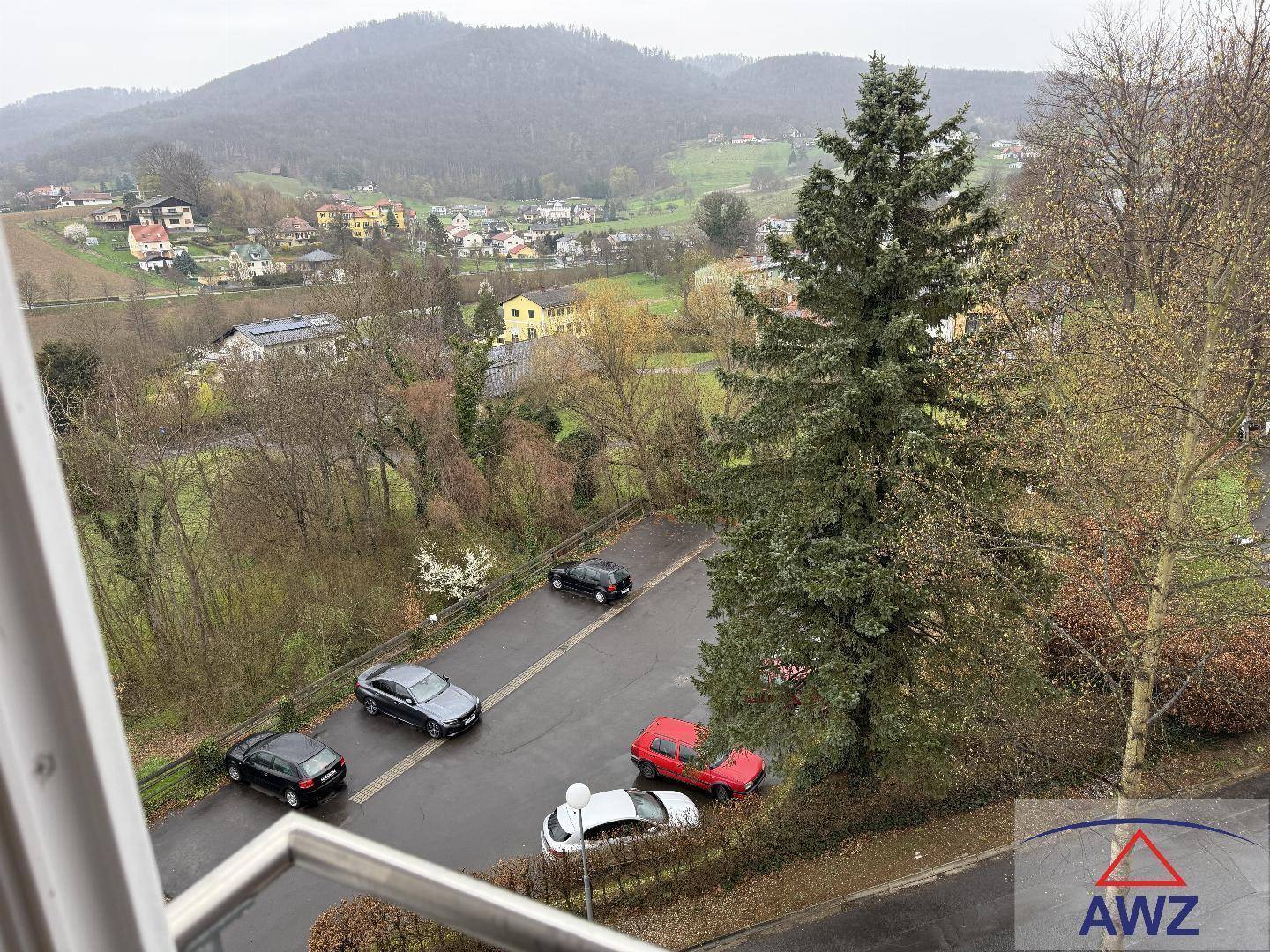 Aussicht vom Balkon auf die umliegende Landschaft mit Bäumen und Bergen im Hintergrund.