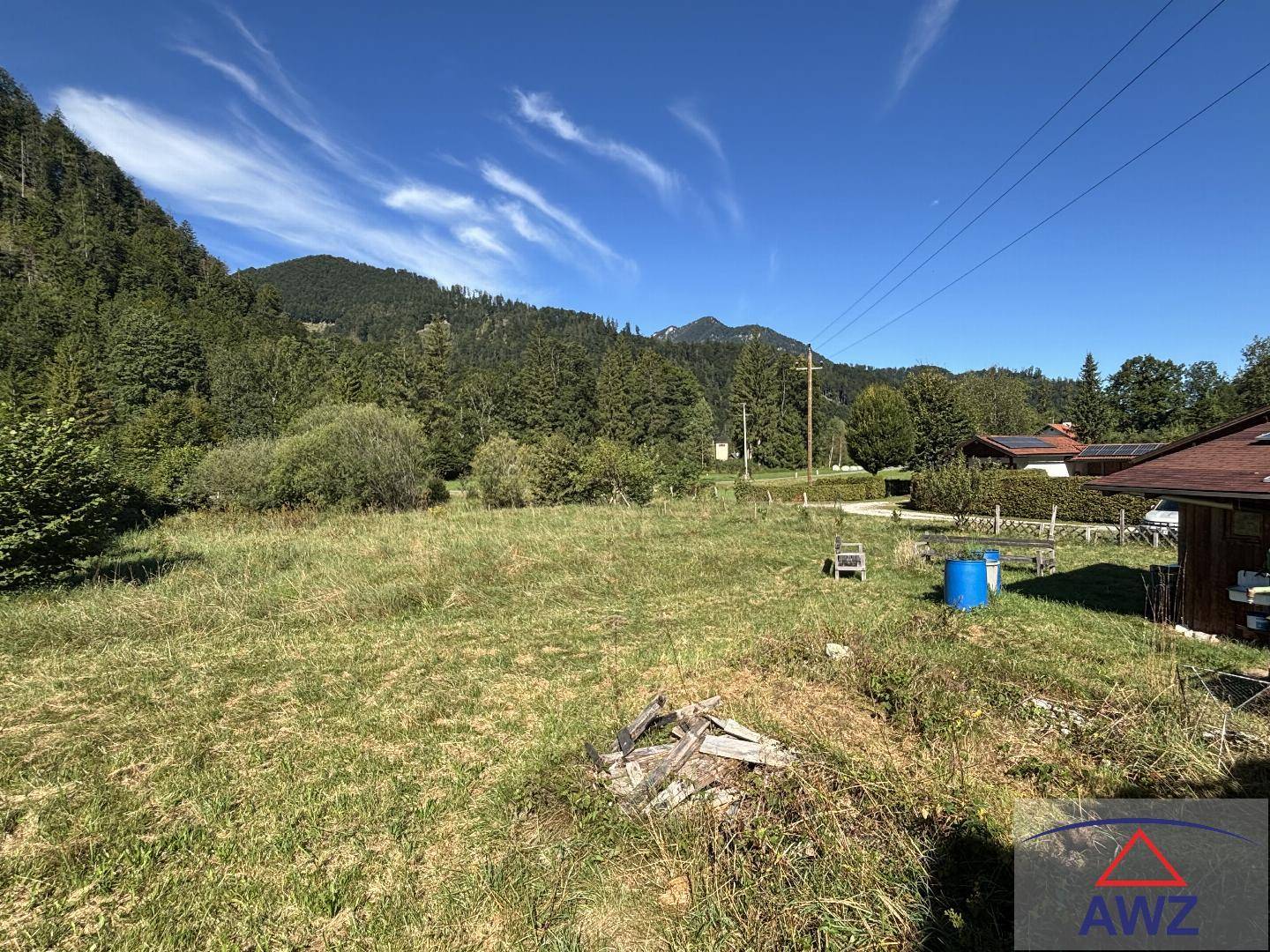 Offene Grasfläche mit Blick auf bewaldete Berge und einige Häuser in der Ferne.