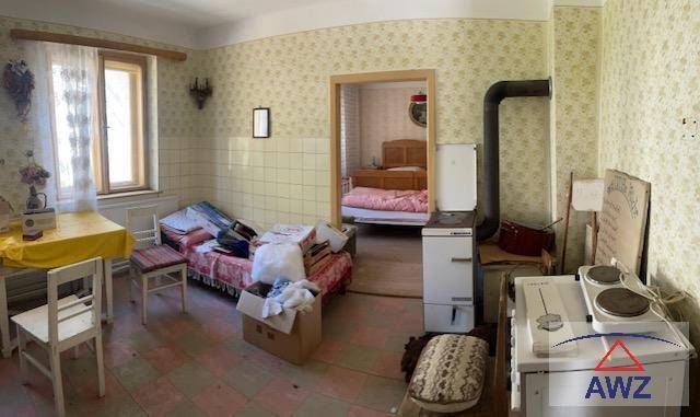 Einfacher Raum mit Ofenheizung, kleinem Tisch und Blick in ein angrenzendes Schlafzimmer.