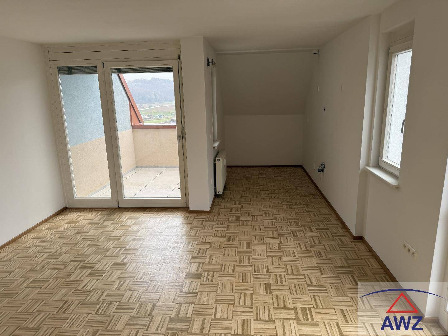 Geräumiger Wohnbereich mit Parkettboden, großen Fenstern und Zugang zu einem Balkon.