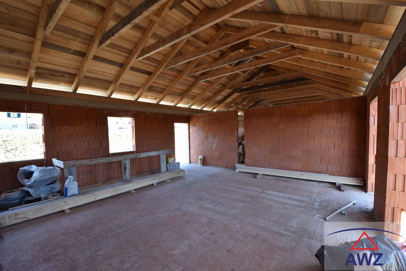 Innenansicht des Rohbaus mit sichtbaren Ziegelwänden und offener Holz-Dachkonstruktion.