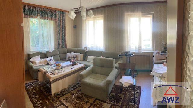 Gemütliches Wohnzimmer mit Ecksofa, Teppichboden und zwei Fenstern für natürliches Licht.