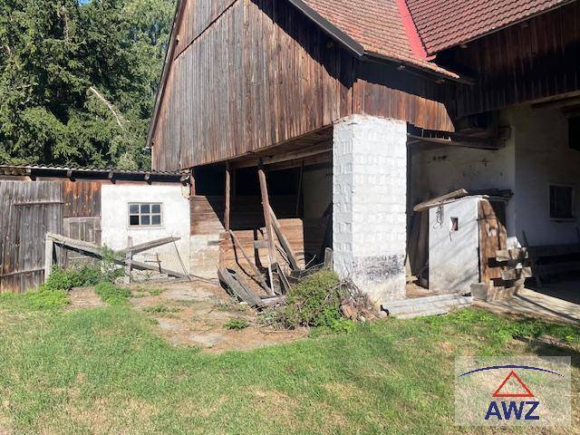 Rustikales Nebengebäude mit Holzwänden und Ziegeldach, umgeben von viel Grün.