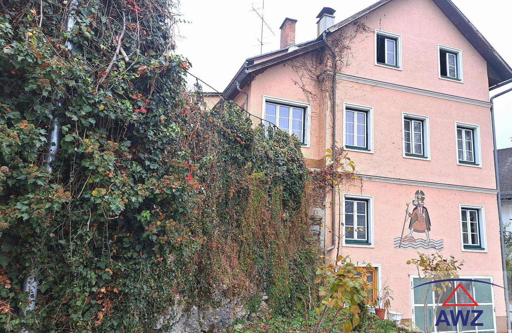 Seitenansicht des Gebäudes mit üppigem Efeu an der Wand und einer historischen Fassadenmalerei.