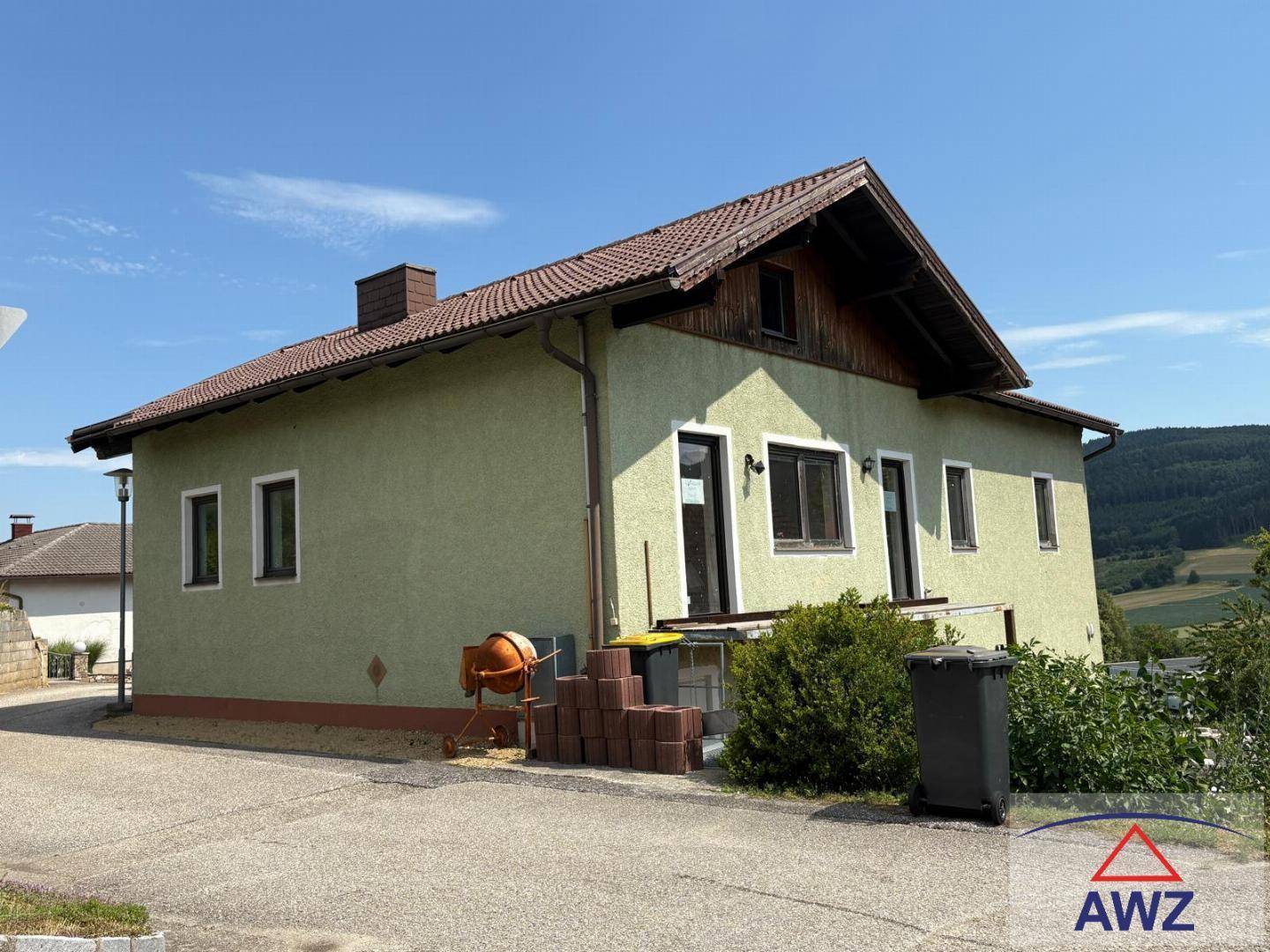 Einfamilienhaus mit grüner Fassade, Satteldach und Blick auf die umliegende Landschaft.